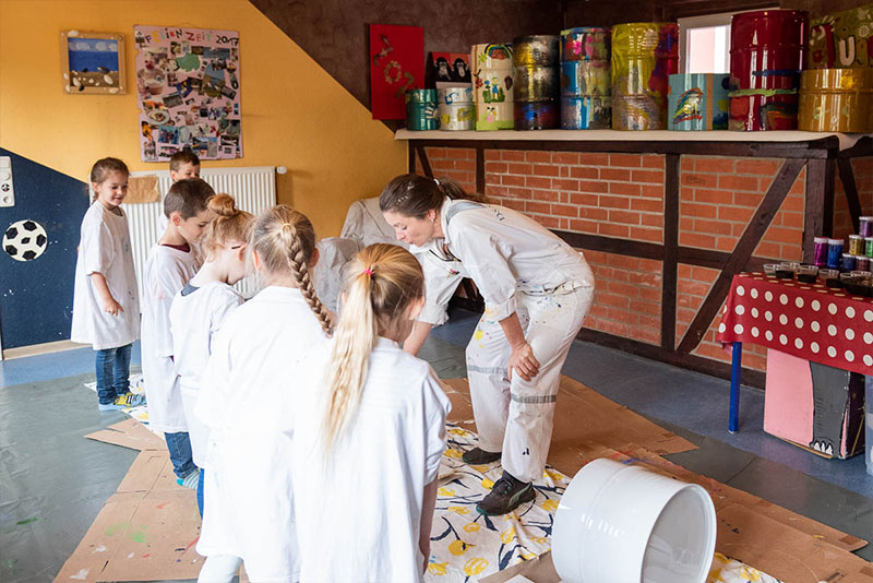 Künstlerin Tila bemalt mit Kindern Metalltonnen